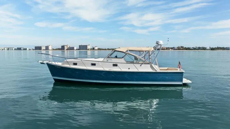 Whattakeeper Yacht Photos Pics 2006 Mainship 34 Rum Runner II boat on calm water with city skyline background.