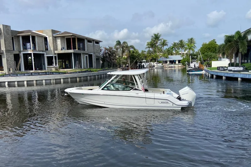 Yacht Photos Pics 2021 Boston Whaler 280 Vantage cruising in a scenic canal with modern homes.