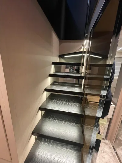  Yacht Photos Pics Modern staircase inside 2024 Cranchi Sessantasette 67 yacht, featuring sleek black steps and mirrored wall.