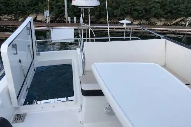 Sweet & Salty Yacht Photos Pics 2019 Jeanneau Velasco 37F yacht deck with seating and table, docked by lush greenery.