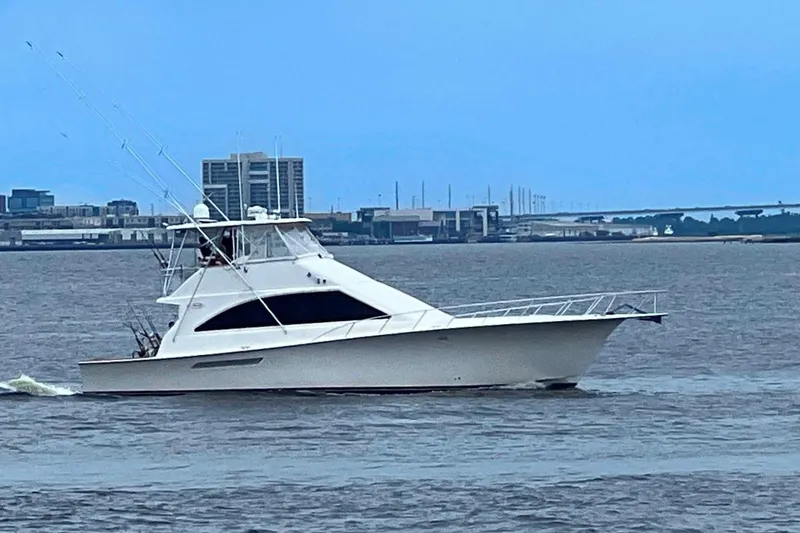 Reel Interest Yacht Photos Pics 2002 Ocean Yachts 56 Super Sport cruising on a calm waterway with cityscape background.