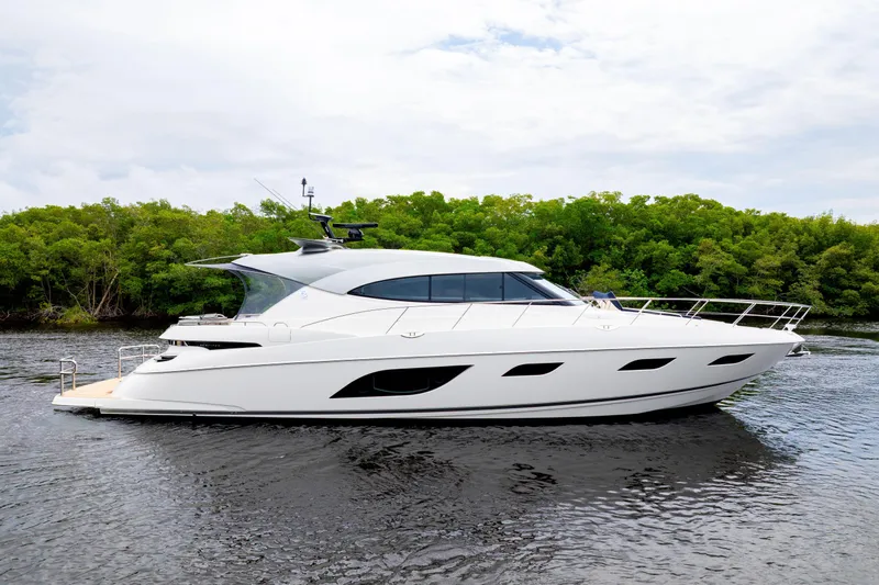  Yacht Photos Pics 2026 Riviera 6000 Sport Yacht cruising on a serene river with lush greenery.