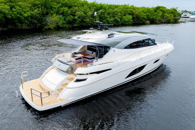  Yacht Photos Pics 2026 Riviera 6000 Sport Yacht cruising on a serene river, surrounded by lush greenery.