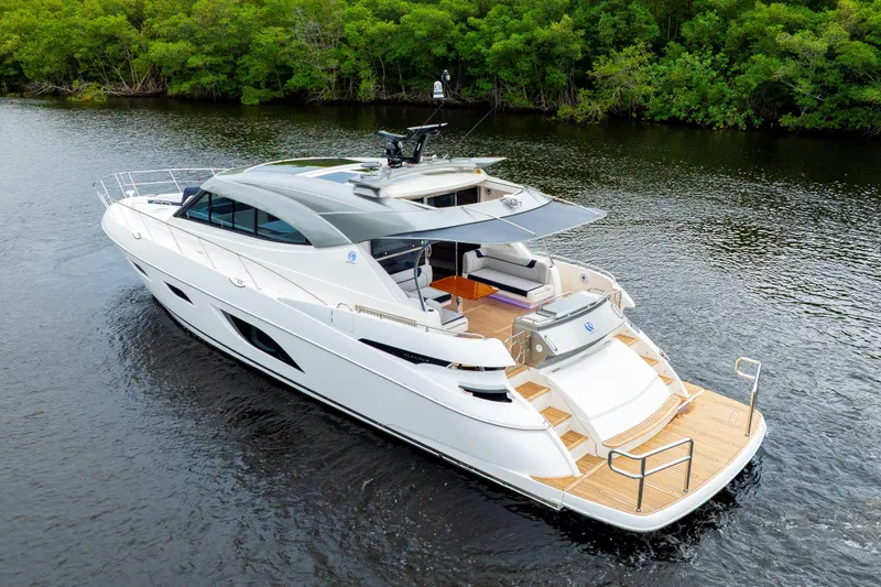  Yacht Photos Pics 2026 Riviera 6000 Sport Yacht cruising on a serene river, surrounded by lush greenery.