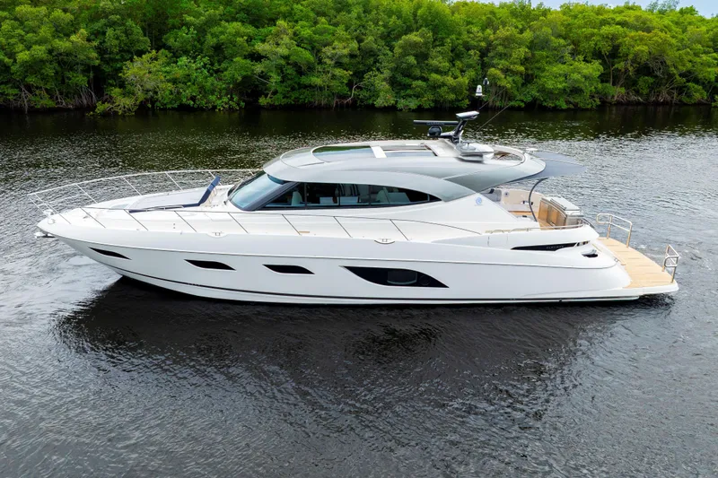  Yacht Photos Pics 2026 Riviera 6000 Sport Yacht cruising on a serene river, surrounded by lush greenery.