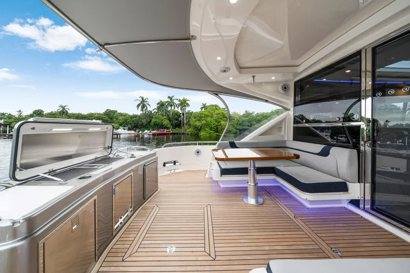  Yacht Photos Pics Luxurious 2026 Riviera 6000 Sport Yacht deck with seating, table, and scenic waterfront view.