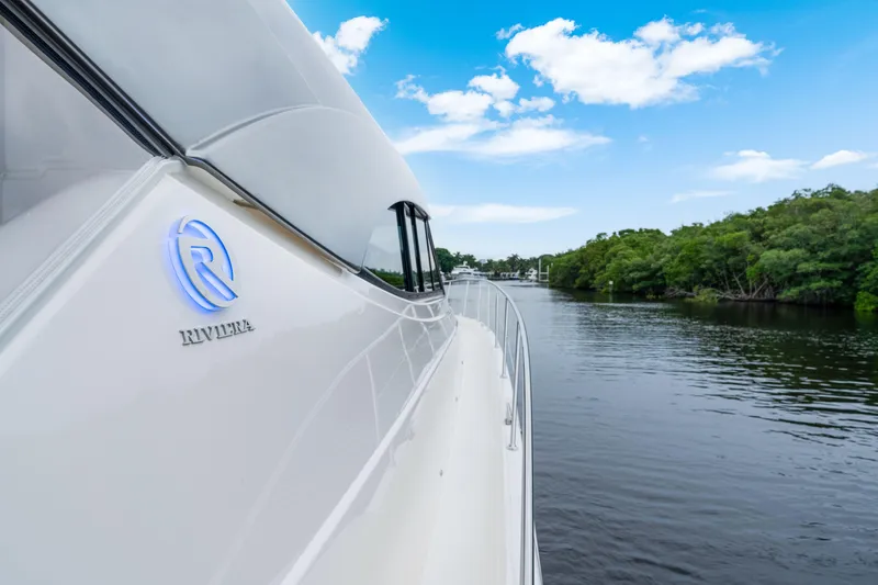  Yacht Photos Pics 2026 Riviera 6000 Sport Yacht cruising on a serene river under a clear blue sky.