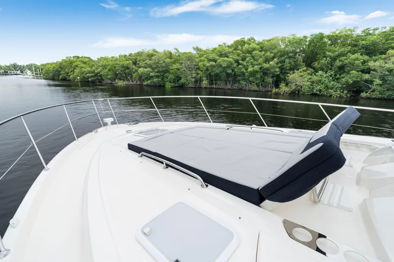  Yacht Photos Pics 2026 Riviera 6000 Sport Yacht with sunbed, cruising on a serene river with lush greenery.