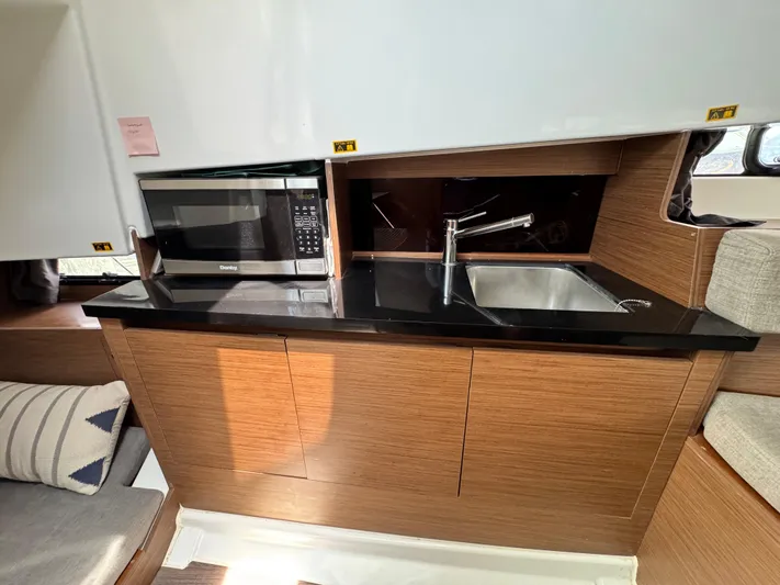  Yacht Photos Pics 2022 Beneteau Flyer 9 SUNdeck interior kitchen with microwave, sink, and wooden cabinetry.