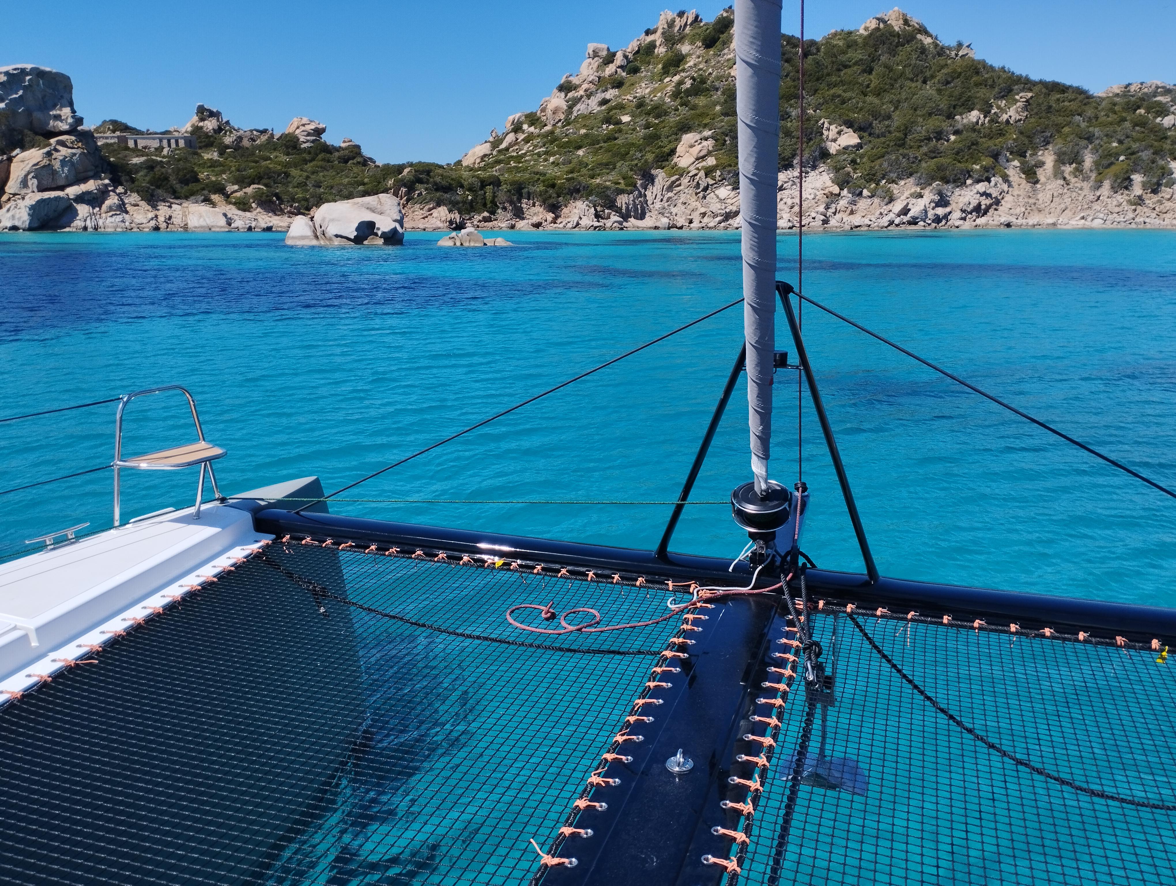 2025 Comar C-Cat 48 catamaran sailing in clear turquoise waters near rocky coastline.