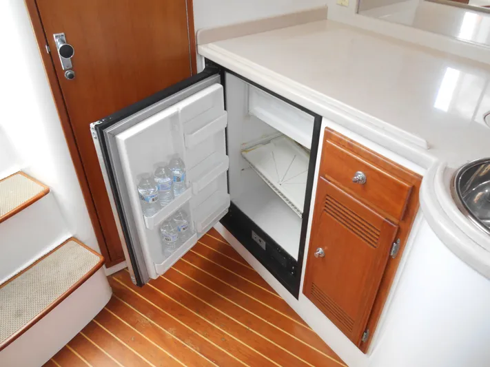 Mistress Yacht Photos Pics 1998 Cabo 31 Express boat interior with open mini fridge and wooden cabinetry.