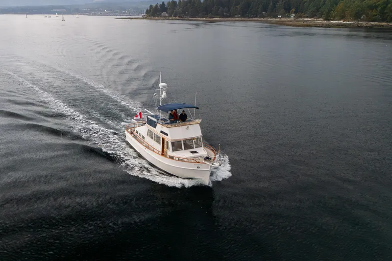  Yacht Photos Pics 1989 Grand Banks 42 cruising on calm waters near a forested shoreline.