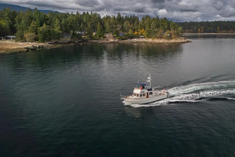  Yacht Photos Pics 1989 Grand Banks 42 cruising near a forested shoreline under cloudy skies.