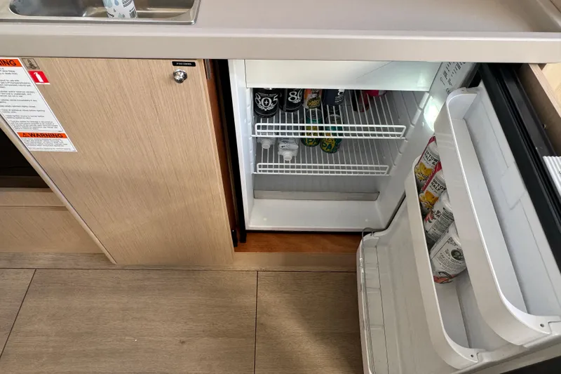  Yacht Photos Pics Compact fridge in 2023 Beneteau Oceanis 38.1 yacht galley, stocked with beverages.