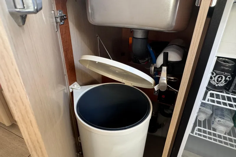 Yacht Photos Pics Under-sink storage on 2023 Beneteau Oceanis 38.1 yacht with trash bin and plumbing.