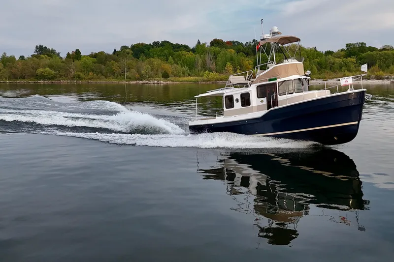  Yacht Photos Pics 2025 Ranger Tugs R-31 CB cruising on a serene lake with lush green shoreline.