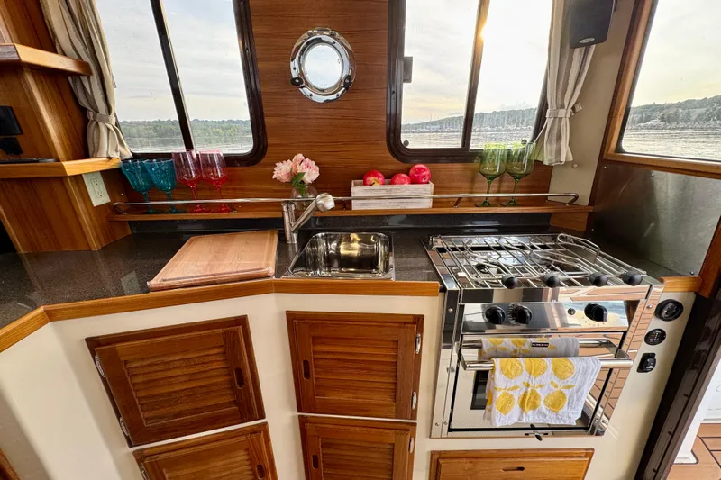  Yacht Photos Pics 2025 Ranger Tugs R-31 CB kitchen with wooden cabinets, stove, and scenic window view.