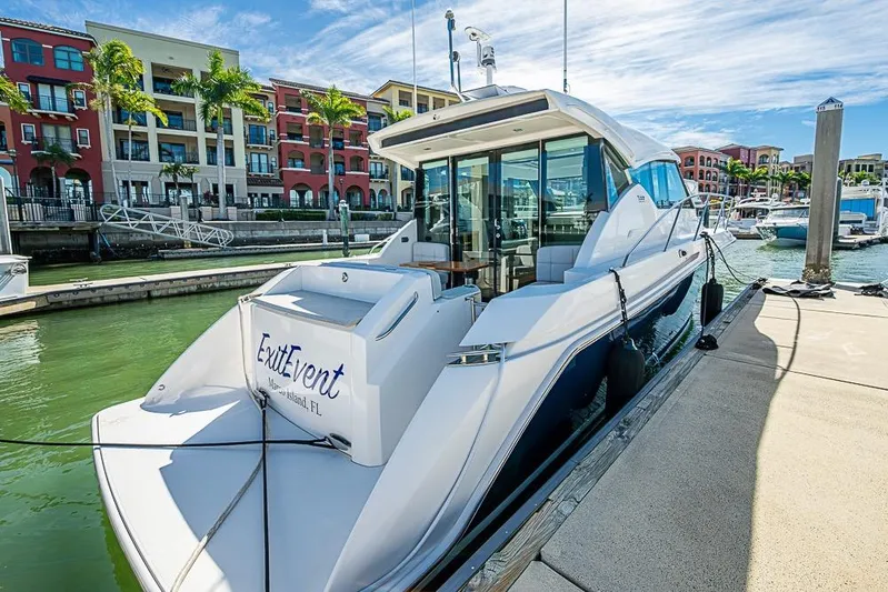 Exitevent Yacht Photos Pics 2017 Tiara Yacht Coupe docked at marina, surrounded by colorful buildings and palm trees.