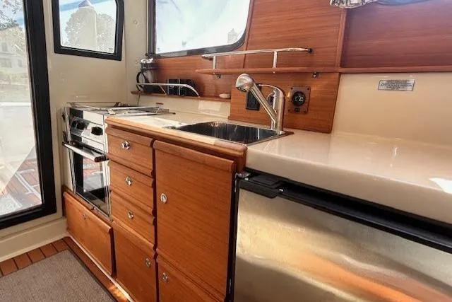  Yacht Photos Pics 2024 Ranger Tugs R-27 interior kitchen with wood cabinetry, sink, and stainless steel appliances.