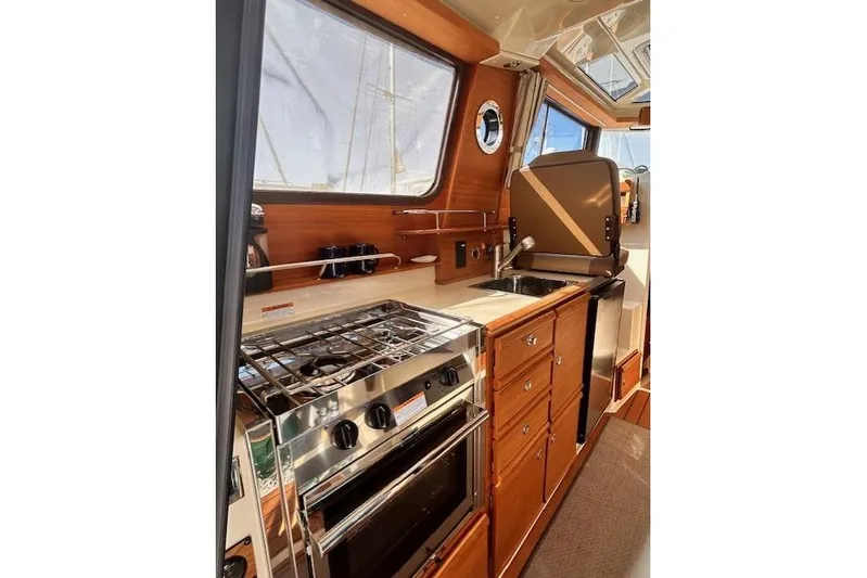  Yacht Photos Pics 2024 Ranger Tugs R-27 interior kitchen with stove, sink, and wooden cabinetry.