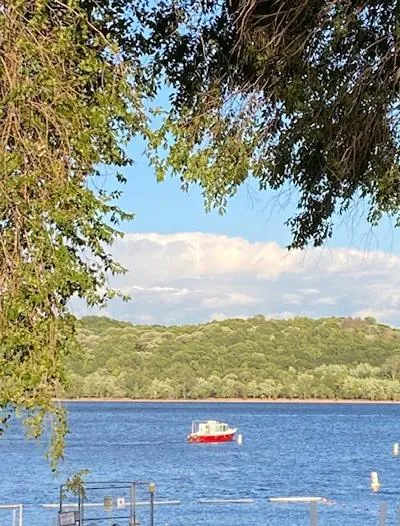  Yacht Photos Pics Red trawler on a serene lake, surrounded by lush greenery and a clear blue sky.