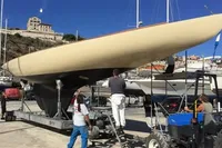 Historic 1905 PLYMS Prototype Sloop on trailer, surrounded by people in a sunny boatyard.