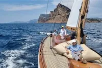 Sailing on 1905 PLYMS PROTOTYPE SLOOP near rocky coastline under clear skies.