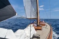 Sailing on a 1905 PLYMS PROTOTYPE SLOOP, wooden deck, open sea, clear sky.