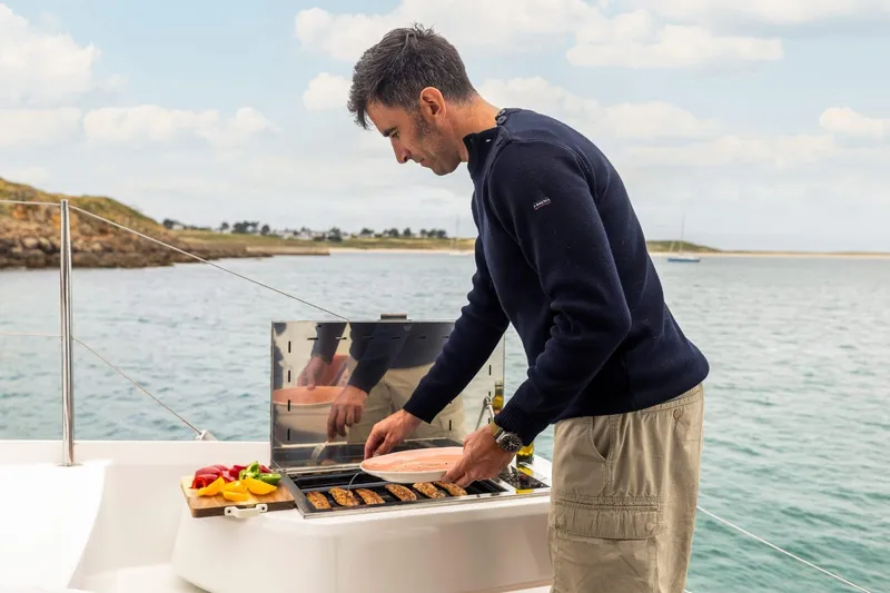  Yacht Photos Pics Man grilling on Fountaine Pajot 41 yacht, 2025 model, with scenic ocean backdrop.