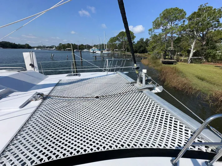 Sola Fide Yacht Photos Pics Catamaran deck with netting, Russell Yachts Crowther 1993, docked by a scenic shoreline.