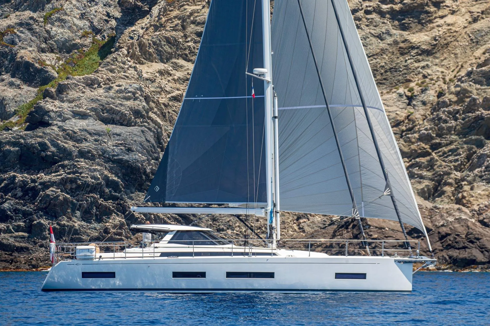 2023 Amel 50 yacht sailing near rocky coastline.