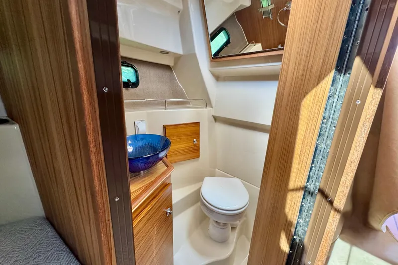  Yacht Photos Pics 2025 Ranger Tugs R-27 boat bathroom with wooden cabinetry and blue glass sink.