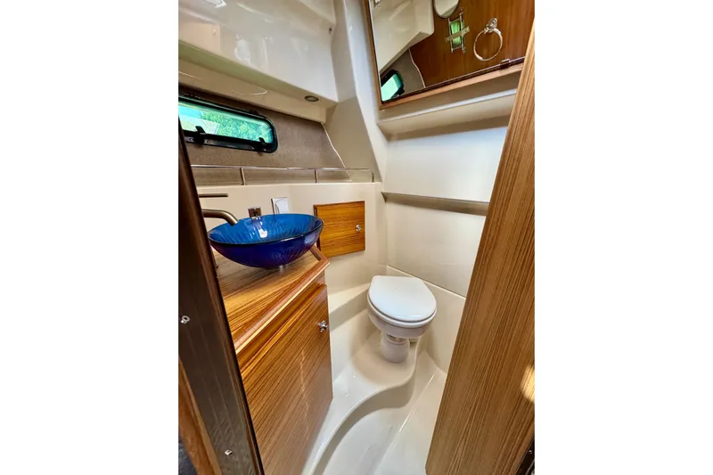  Yacht Photos Pics 2025 Ranger Tugs R-27 boat bathroom with blue glass sink and wooden cabinetry.
