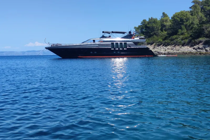  Yacht Photos Pics Luxurious 1992 Posillipo Technema 82 yacht anchored in serene blue waters near a forested coastline.