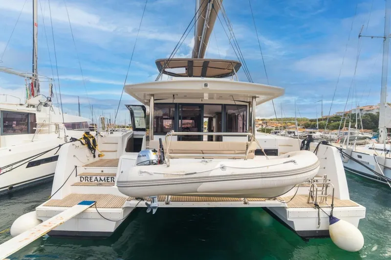 Dreamer Yacht Photos Pics 2022 Bali 4.6 catamaran docked with inflatable boat, clear sky, marina setting.