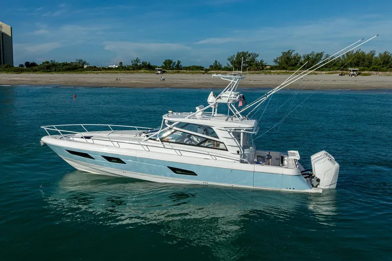 Rising Tide Yacht Photos Pics 2023 Intrepid 477 Evolution yacht cruising on clear blue water near a sandy beach.