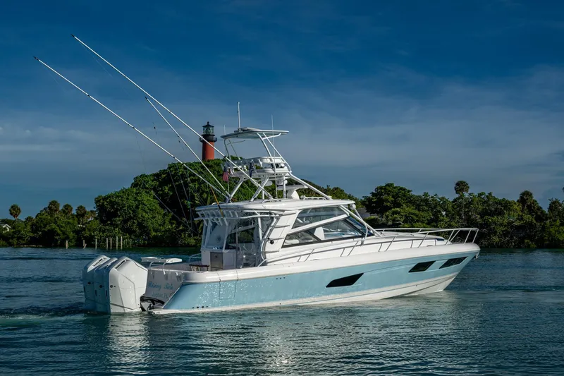 Rising Tide Yacht Photos Pics 2023 Intrepid 477 Evolution boat cruising near a lighthouse, surrounded by lush greenery.