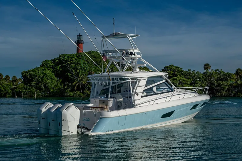 Rising Tide Yacht Photos Pics 2023 Intrepid 477 Evolution yacht cruising near a lighthouse, surrounded by lush greenery.