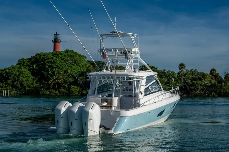 Rising Tide Yacht Photos Pics 2023 Intrepid 477 Evolution boat cruising near a lighthouse, surrounded by lush greenery.