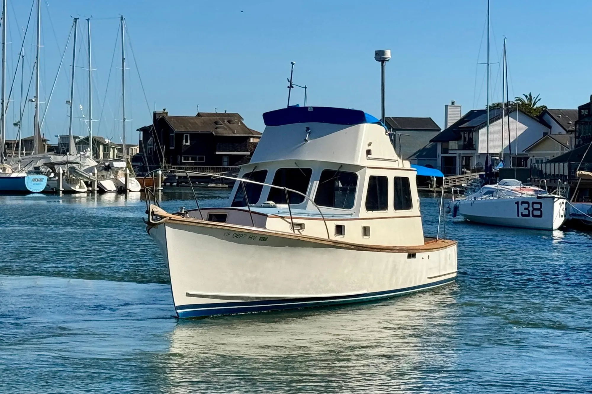 1982 Jarvis Newman Flybridge Cruiser in marina, surrounded by sailboats and waterfront homes.