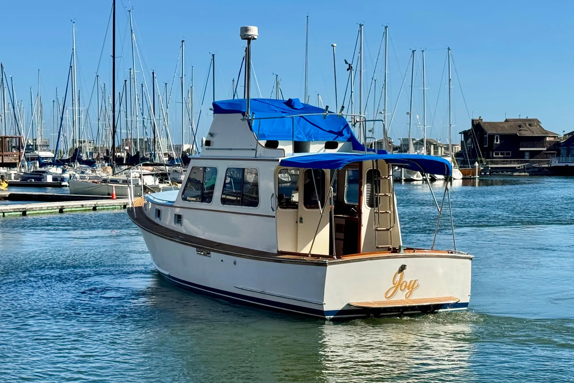 1982 Jarvis Newman Flybridge Cruiser in marina, blue canopy, named "Joy".