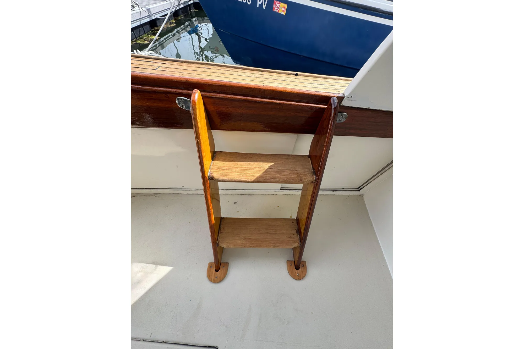 Wooden ladder on 1982 Jarvis Newman Flybridge Cruiser, docked near a blue boat.
