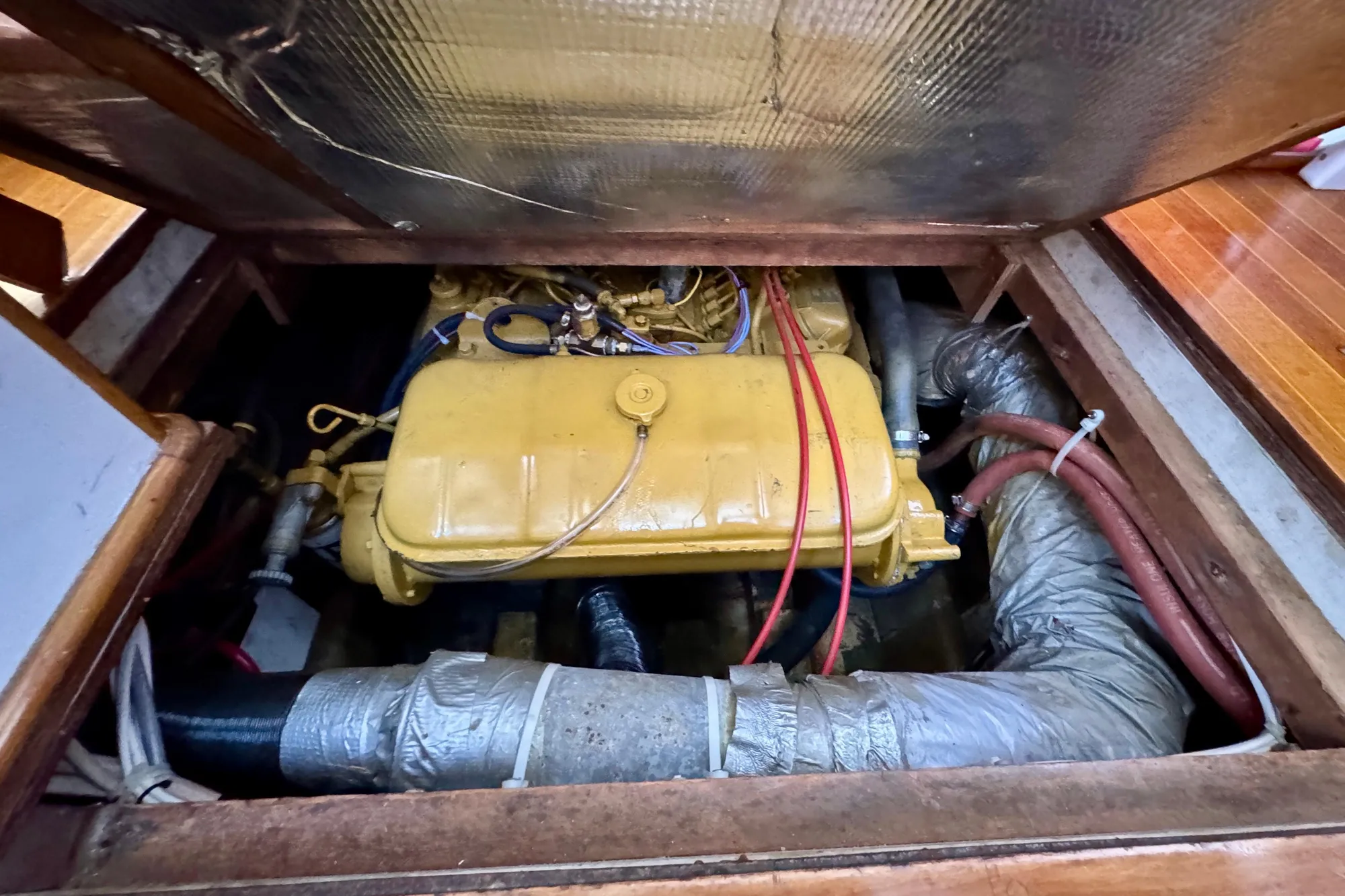 1982 Jarvis Newman Flybridge Cruiser engine compartment with yellow engine and red hoses.