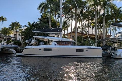 2019 Lagoon 42 catamaran docked by palm trees, reflecting sunlight on water.