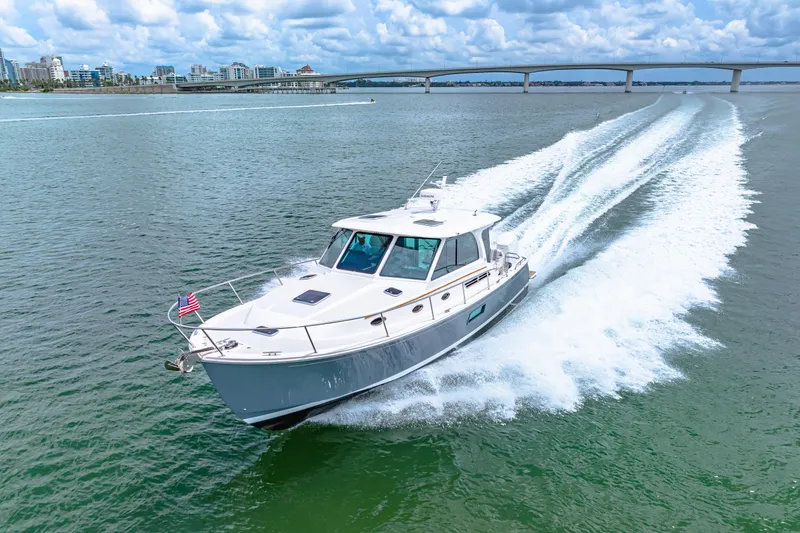 Yacht Photos Pics 2024 Back Cove 39O cruising on water with cityscape and bridge in background.