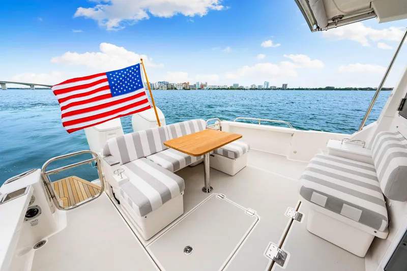  Yacht Photos Pics 2024 Back Cove 39O yacht deck with seating, table, and American flag, overlooking water.