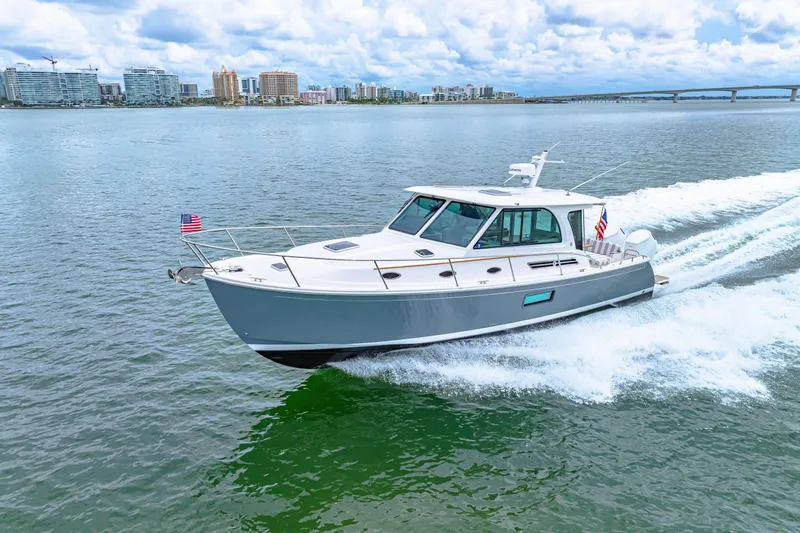  Yacht Photos Pics 2024 Back Cove 39O cruising on water with city skyline in background.