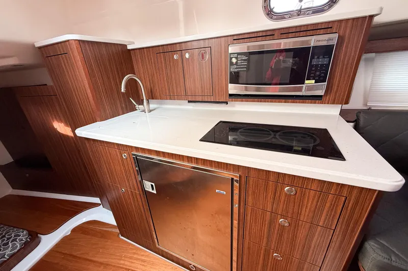  Yacht Photos Pics 2016 Pursuit OS 355 Offshore yacht kitchen with wood cabinetry, sink, microwave, and stovetop.