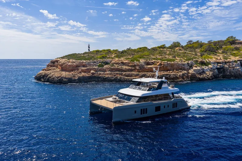 Vahewa Yacht Photos Pics 2024 Sunreef Power Cat cruising near rocky coastline under a clear blue sky.