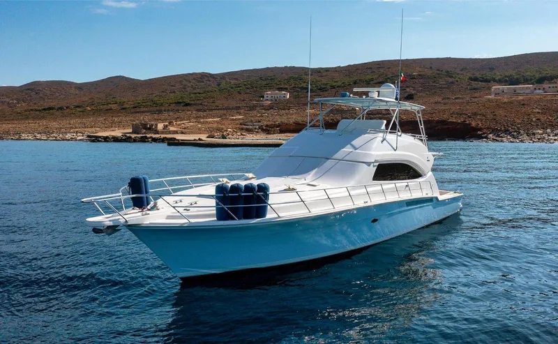  Yacht Photos Pics 2006 Bertram 570 yacht on calm water near rocky shoreline.
